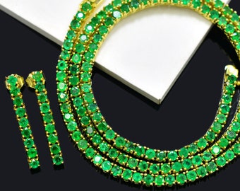 Op de afbeelding: Een gouden ketting en bijpassende oorbellen met smaragdgroene edelstenen. De ketting is een dikke ketting met meerdere rijen smaragdstenen.
