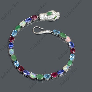Pode incluir: Um bracelete de cobra de prata com um fecho de cabeça de cobra. O bracelete é adornado com uma variedade de pedras preciosas, incluindo esmeralda, opala, rubi, safira e topázio.
