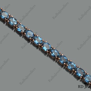 May include: A delicate silver chain bracelet with a row of light blue oval-shaped gemstones. The bracelet is made of sterling silver and features a classic design.