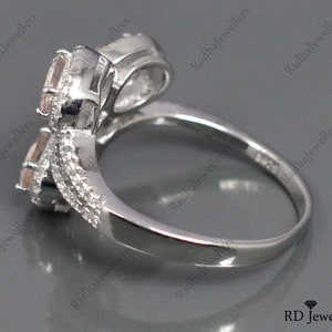May include: A silver ring with two pink gemstones set in a twisted band. The ring is designed to be worn on the knuckle.