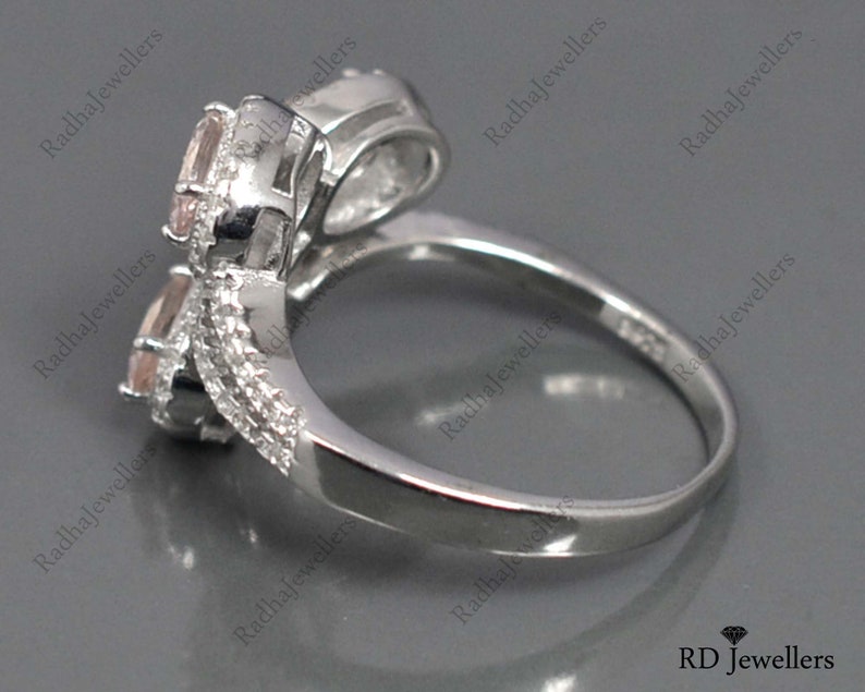 May include: A silver ring with two pink gemstones set in a twisted band. The ring is designed to be worn on the knuckle.