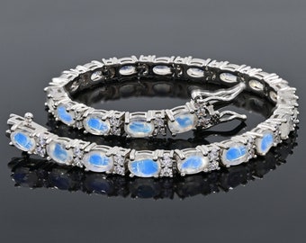 Puede incluir: Una pulsera de plata con gemas de piedra lunar ovaladas y piedras redondas transparentes más pequeñas. La pulsera tiene un cierre de broche.