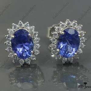 May include: A pair of silver earrings with a blue oval gemstone surrounded by a halo of smaller white gemstones.