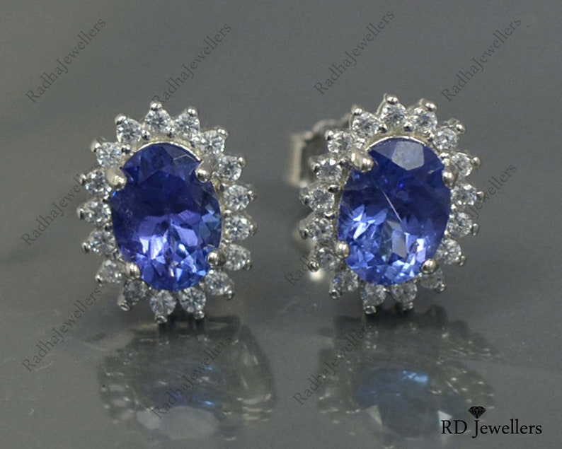May include: A pair of silver earrings with a blue oval gemstone surrounded by a halo of smaller white gemstones.