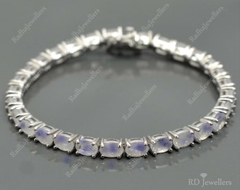 Puede incluir: Un brazalete de plata con una fila de piedras de luna ovaladas. El brazalete está hecho de una cadena delicada con un cierre de broche.
