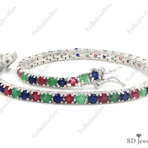 May include: A silver bracelet with alternating red, green, and blue gemstones. The bracelet is made of small, square links and has a clasp closure. The gemstones are round and set closely together.