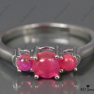 May include: A silver ring with three pink gemstones. The ring is set with three round stones, each with a smooth, polished surface. The stones are set in a prong setting, which allows the light to reflect off of the stones from all angles.