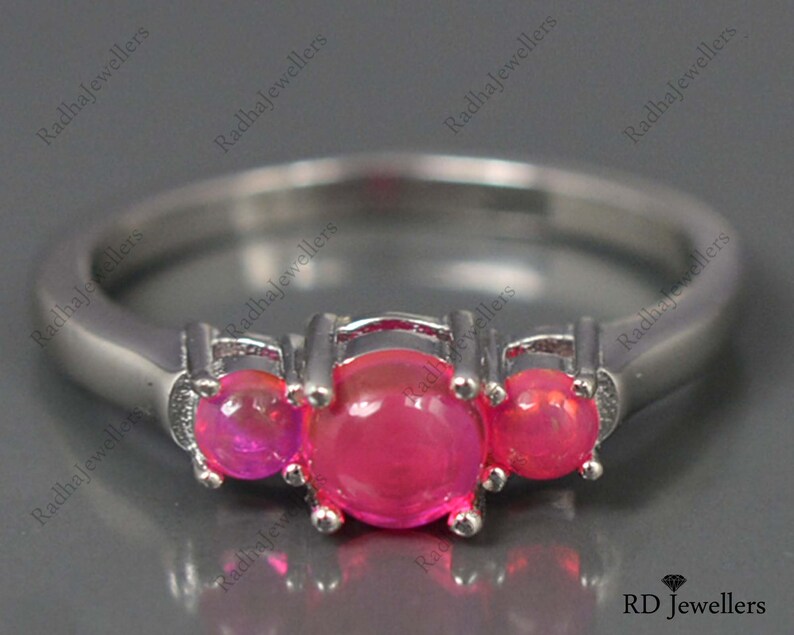 May include: A silver ring with three pink gemstones. The ring is set with three round stones, each with a smooth, polished surface. The stones are set in a prong setting, which allows the light to reflect off of the stones from all angles.