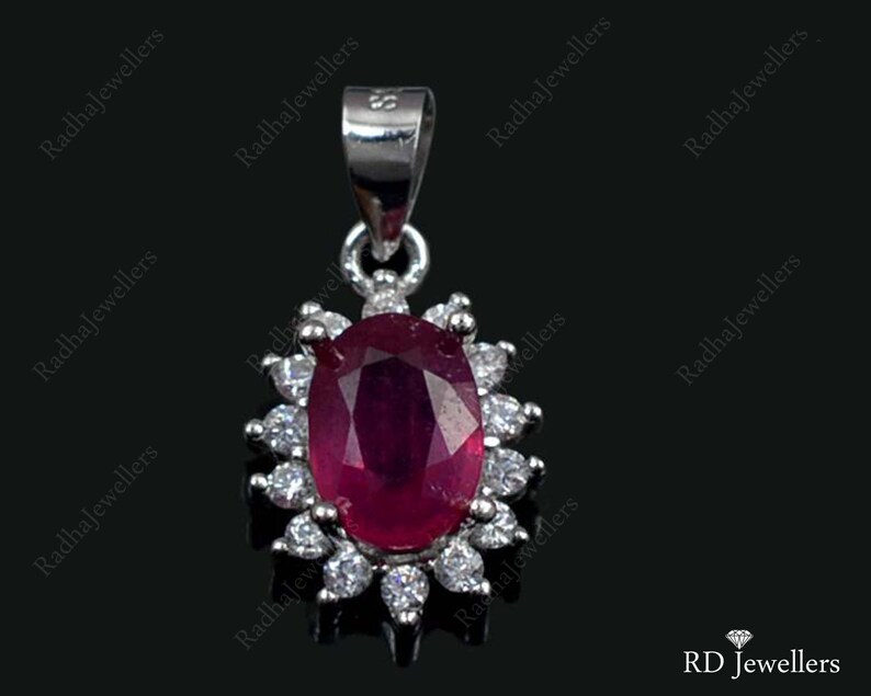 Pu&ograve; includere: Un ciondolo d'argento con una grande pietra di rubino ovale circondata da piccole pietre bianche. Il ciondolo &egrave; incastonato in una cornice d'argento con un design delicato.