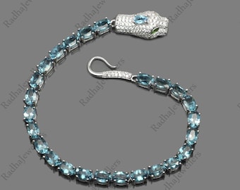 Può includere: Un braccialetto a forma di serpente in argento con un design di pietre preziose blu chiaro. La testa del serpente è dettagliata con zirconi cubici bianchi e occhi verdi.