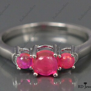 May include: A silver ring with three pink gemstones. The ring is set with three round stones, each with a smooth, polished surface. The stones are set in a prong setting, which allows the light to reflect off of the stones from all angles.