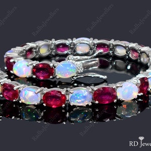 May include: A silver bracelet featuring alternating white opal and red ruby gemstones. The bracelet has a clasp fastening.