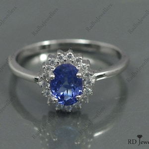 May include: A silver ring with a blue oval gemstone surrounded by smaller white gemstones. The ring is set in a halo style.