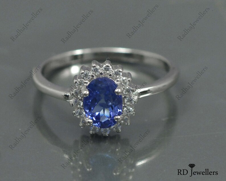 May include: A silver ring with a blue oval gemstone surrounded by smaller white gemstones. The ring is set in a halo style.