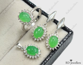 Op de afbeelding: Een set met een groene edelsteenring, oorbellen en een hangerketting met een zilveren setting en heldere zirkonia-stenen. De sieraden worden gepresenteerd in een zwarte fluwelen doos.