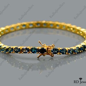 May include: A gold tennis bracelet with a row of blue gemstones. The bracelet has a clasp closure.