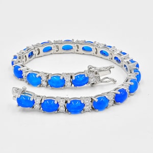 Op de afbeelding: Een zilveren tennisarmband met blauwe ovale stenen en heldere ronde stenen.