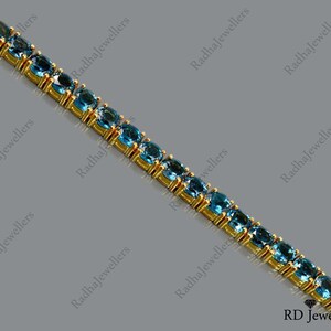 May include: A gold chain bracelet with blue gemstones. The bracelet is made of small, oval-shaped gemstones set in a gold chain.