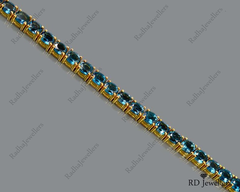 May include: A gold chain bracelet with blue gemstones. The bracelet is made of small, oval-shaped gemstones set in a gold chain.