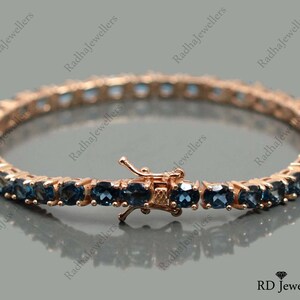 May include: A rose gold tennis bracelet with blue topaz stones. The bracelet has a secure clasp.