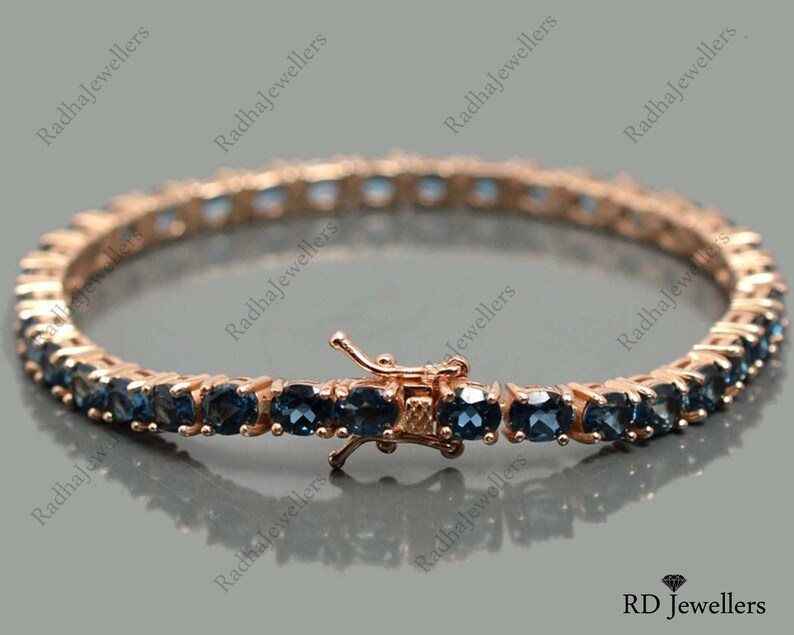 May include: A rose gold tennis bracelet with blue topaz stones. The bracelet has a secure clasp.