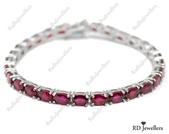 May include: A silver tennis bracelet featuring a row of oval-shaped ruby gemstones.