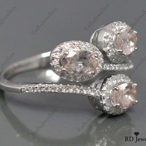 May include: A silver ring with three oval-shaped pink gemstones set in a halo of smaller clear gemstones. The ring has a twisted band.