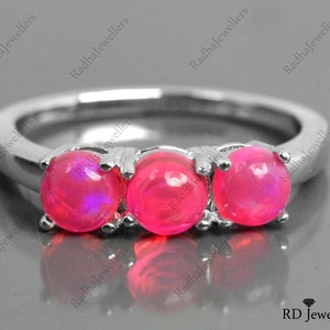 May include: A silver ring with three pink opal stones set in a row. The ring is on a gray background.