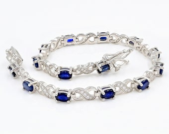 May include: A silver bracelet with a delicate infinity design and oval-shaped blue gemstones. The bracelet is adorned with smaller clear gemstones.