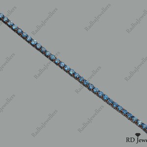 May include: A delicate blue gemstone tennis bracelet with a silver clasp. The bracelet is made of small, oval-shaped gemstones set in a silver chain.