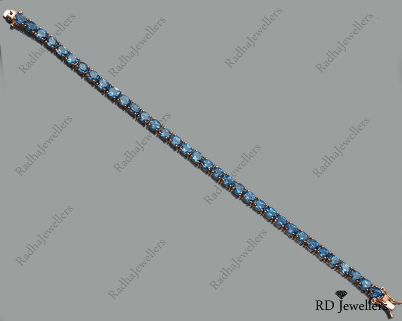 May include: A delicate blue gemstone tennis bracelet with a silver clasp. The bracelet is made of small, oval-shaped gemstones set in a silver chain.