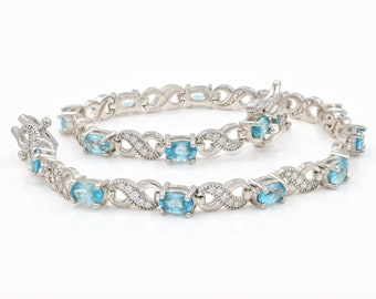 Può includere: Un braccialetto d'argento con un delicato design a infinito e pietre ovali blu. Il braccialetto è incastonato con pietre trasparenti più piccole.