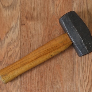 May include: A hammer with a wooden handle and a black metal head. The hammer is lying on a wooden surface.