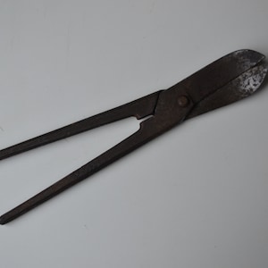 以下が含まれることがあります： 長いハンドルが付いたさびた金属製のハサミ。ハサミが開いていて、切る準備ができています。