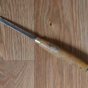 May include: A wooden handled chisel with a metal blade. The handle is worn and has a brass ferrule.