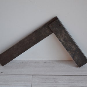 Peut inclure: Une équerre de charpentier en métal rouillé avec un angle de 90 degrés.