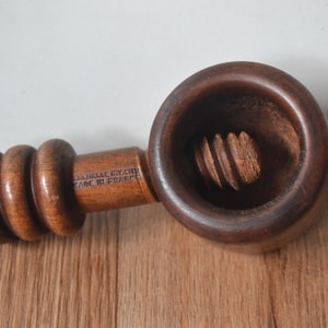 Peut inclure: Un casse-noix en bois vintage avec une finition marron foncé. Le casse-noix a une section en forme de bol rond et une poignée avec trois sections arrondies. Le texte "MADE IN FRANCE" est visible sur la poignée.