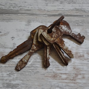 May include: A bunch of old, rusty keys with white painted handles. The keys are piled together on a white wooden surface.