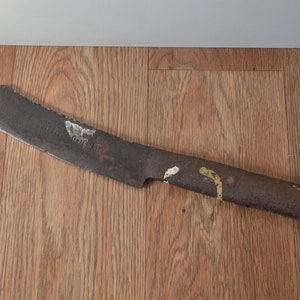 May include: A rusty, curved blade with a wooden handle. The blade has a faded inscription on it.