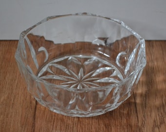 May include: A clear glass bowl with a geometric pattern. The bowl has a wide, round shape and a slightly flared rim.