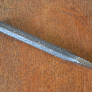 May include: A silver metal chisel with a rounded head and a pointed tip. The chisel is marked "MADE IN ENGLAND".