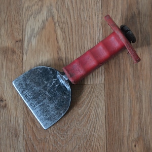 May include: A red-handled metal tool with a rounded blade, used for scraping or smoothing surfaces.