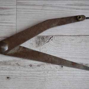 May include: A rusty metal compass with a brass screw and a pointed tip. The compass is on a white wooden surface.