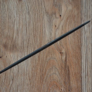 May include: A long, thin, black metal file on a wooden surface.