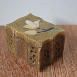 May include: A small, intricately carved green stone box with a floral design on the top. The box is made of soapstone and has a hinged lid.