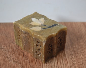 May include: A small, intricately carved green stone box with a floral design on the top. The box is made of soapstone and has a hinged lid.