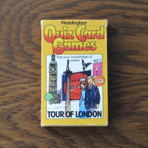 Könnte beinhalten: Gelbe Schachtel mit Waddington's Quiz Card Games, Tour of London. Die Schachtel zeigt Illustrationen von Big Ben, einem Paar und einem Schmetterling. Der Text auf der Schachtel lautet "Testen Sie Ihr Wissen über London."