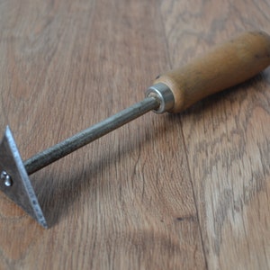 May include: A scraper with a wooden handle and a triangular metal blade. The blade is slightly curved and has a small hole in the centre.