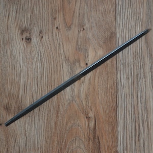 Puede incluir: Una lima de metal larga, delgada y de color plateado.