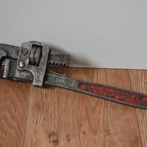 May include: A vintage, silver-coloured pipe wrench with a red handle. The wrench has a 10-inch capacity and is marked "10" on the handle.